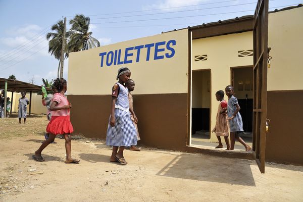 Kinder schauen sich eine neu errichtete, öffentliche Toilette an.