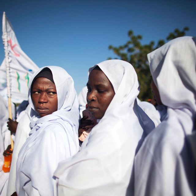 Mehrere sudanesische Frauen in weißer Kleidung schauen in die Kamera und tragen Banner.