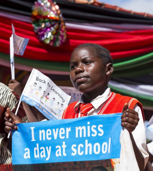 Ein afrikanisches Kind in Schuluniform hält ein Schild "I never miss a day at school".