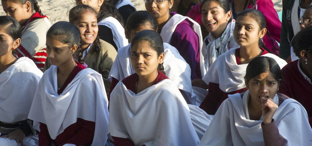 Junge Frauen mit Tüchern um die Schultern sitzen in drei Reihen hintereinander.