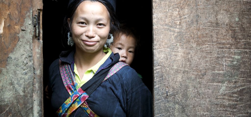 Eine asiatische Frau trägt auf ihrem Rücken ein Kleinkind.