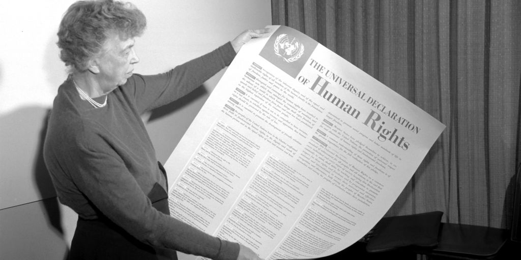 Eleanor Roosevelt hält schräg ein Plakat.