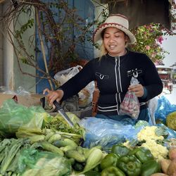 Eine Frau mit Strohhut steht hinter einem Marktstand mit Gemüse.