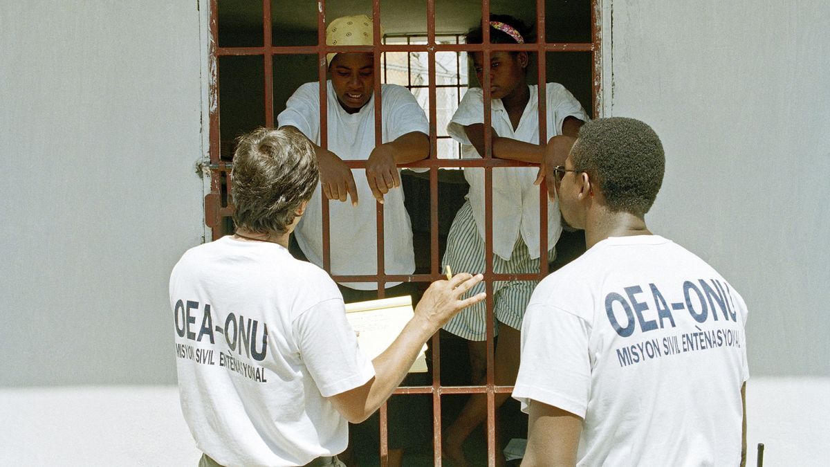 Zwei Frauen werden von UN-Mitarbeitern durch ein vergittertes Fenster befragt.