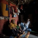 Rohingya refugees in the Kutupalong Rohingya Refugee Camp in Cox's Bazar © UN Photo/KM Asad Drei Rohingya sitzen in einer dunkelen Hütte. Ein Mann, ein Kind und eine Frau. Die Hütte ist dämmerig und ein Lichtschatten fällt auf sie.
