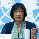 Eine Frau mit kurzen schwarzen Haaren und einer Brille hält vor einem UN-Logo eine Rede