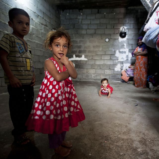 Zwei Kinder und ein Säugling befinden sich in einem geziegelten Unterkunft und schauen in die Kamera