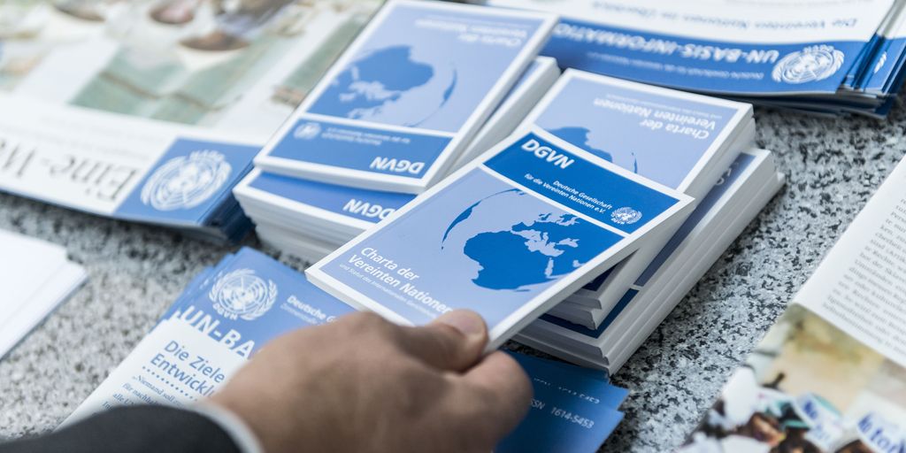 Eine Hand greift ein Exemplar der Charta der Vereinten Nationen von einem Büchertisch.