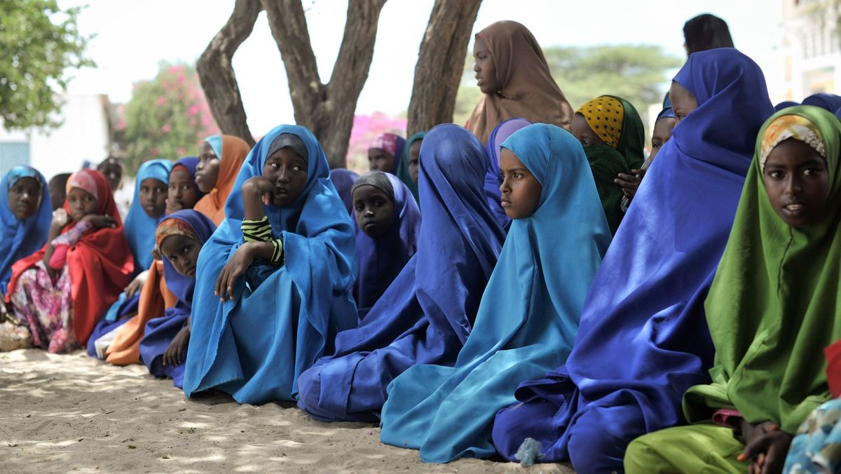 Junge Frauen und Mädchen sitzen in einer Reihe auf dem Boden. Sie tragen Kopftücher und Umhänge. 
