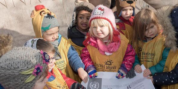 Kinder umringen die Allgemeine Erklärung der Menschenrechte als großen Ausdruck und lächeln in die Kamera.