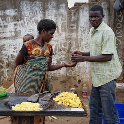 Eine Frau mit Kind auf dem Rücken verkauft einem Mann frittierte Kartoffeln auf einem Markt in Lilongwe, in Malawi.