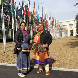Zwei Frauen in langen bunten Rücken stehen vor einigen internationalen Flaggen.