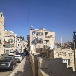 Die große Mehrheit der Geflüchteten lebt nicht in Camps, sondern in Städten wie Amman Eine Straßenansicht von weißen Häusern, in der Ferne das Graffiti eines Frauengesichts